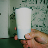Eine Hand hält einen Magic Becher BUNTES *LIMITED EDITION* vor einem Graffiti-Hintergrund und verleiht der farbenfrohen Szene das gewisse Etwas.
