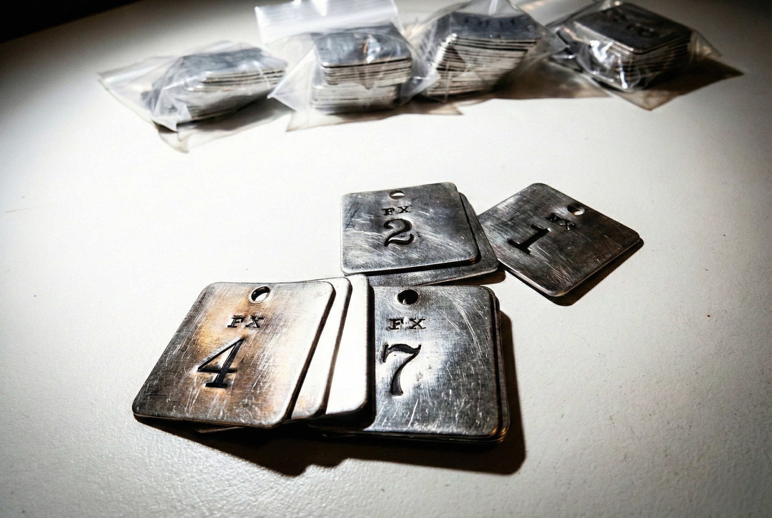 Metallschilder mit Nummern und Löchern, einige in Plastiktüten gestapelt, auf einer weißen Fläche unter hellem Licht.