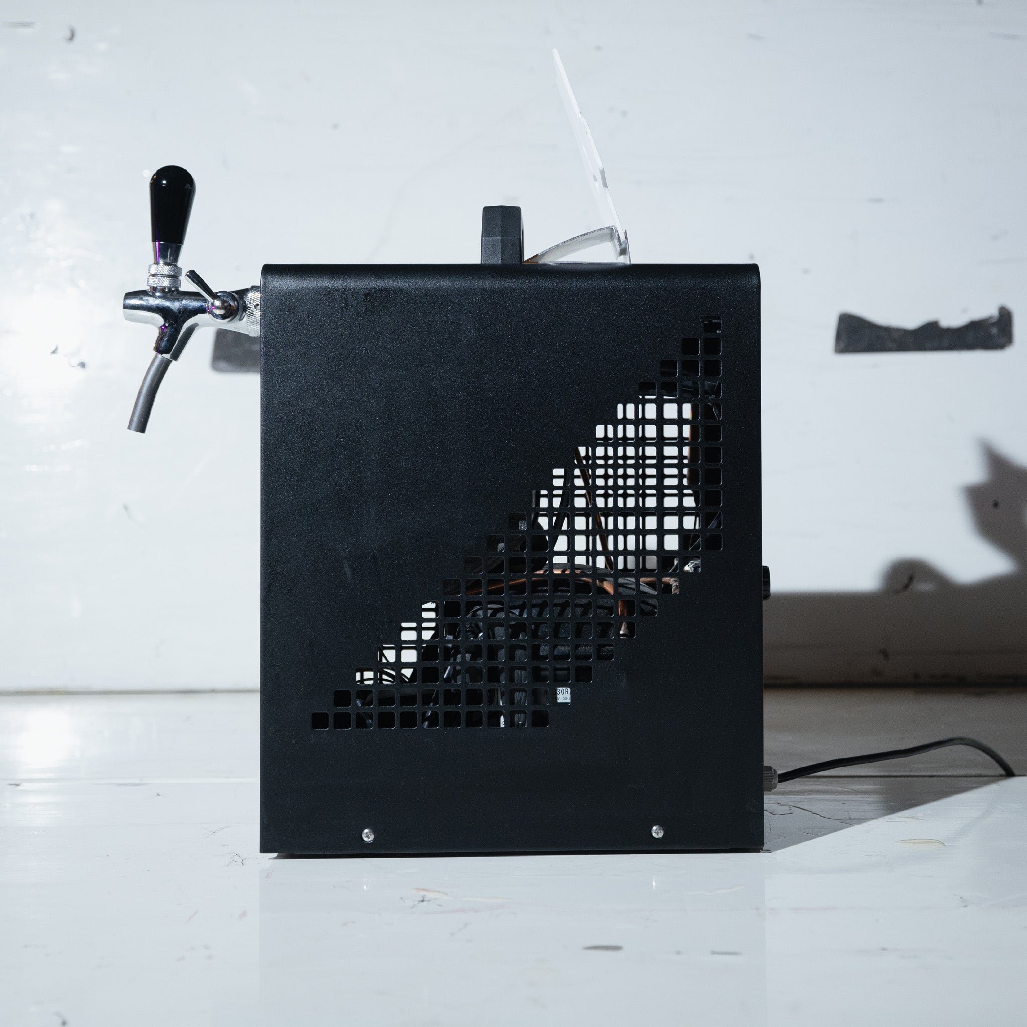 Ein schwarzer Getränkespender mit einem Zapfhahngriff, von der Seite gesehen vor einem weißen Hintergrund.