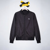 FX Jacke mit reflektierendem Print hängt an einem Holzkleiderbügel unter schwarz-gelbem Band an der Wand.