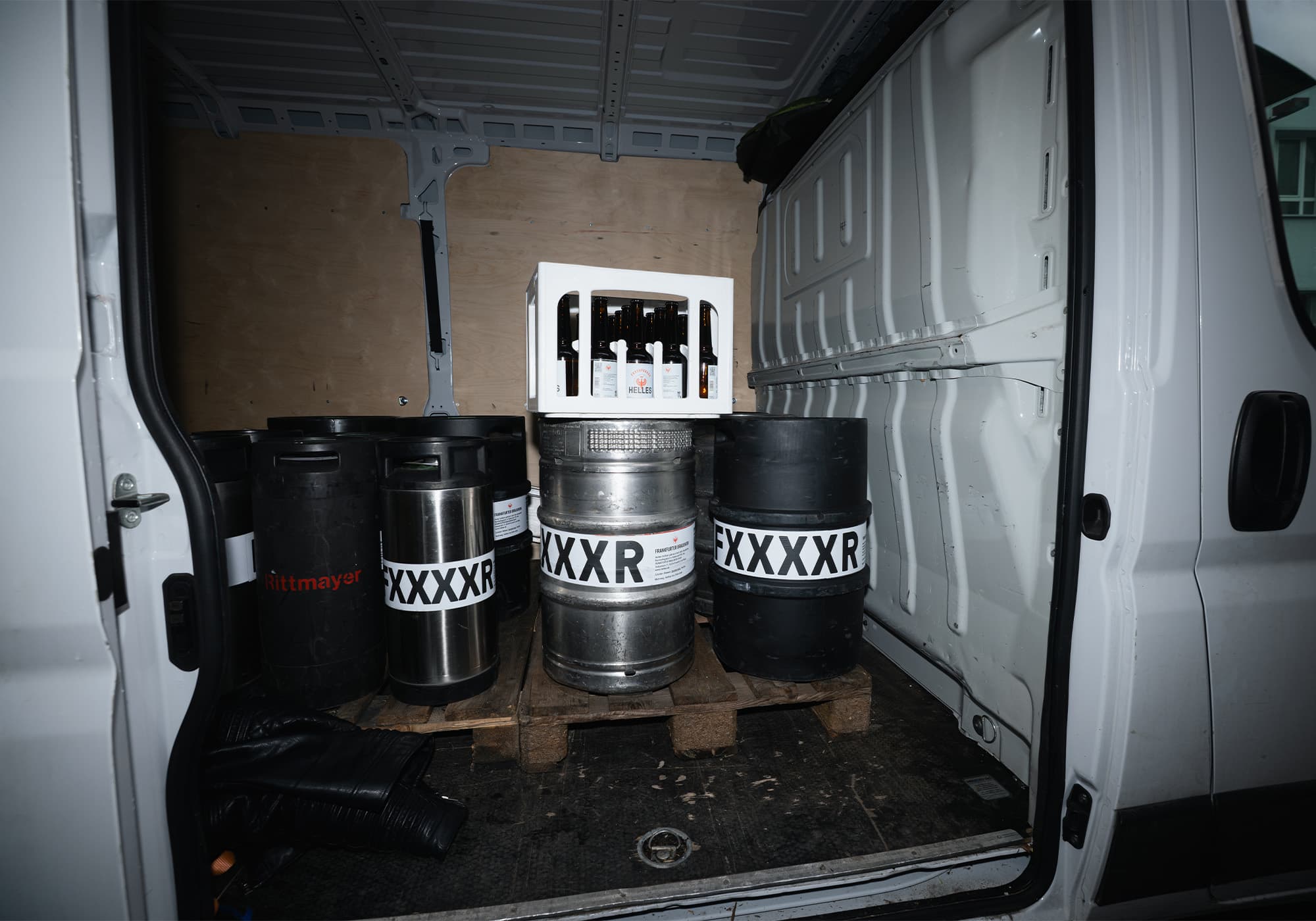 Bierfässer und eine Kiste mit Flaschen auf einer Holzpalette in einem weißen Lieferwagen.