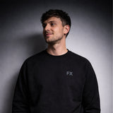 Ein Mann trägt den FX Pulli in Schwarz mit reflektierendem Print und lächelt vor grauem Hintergrund.