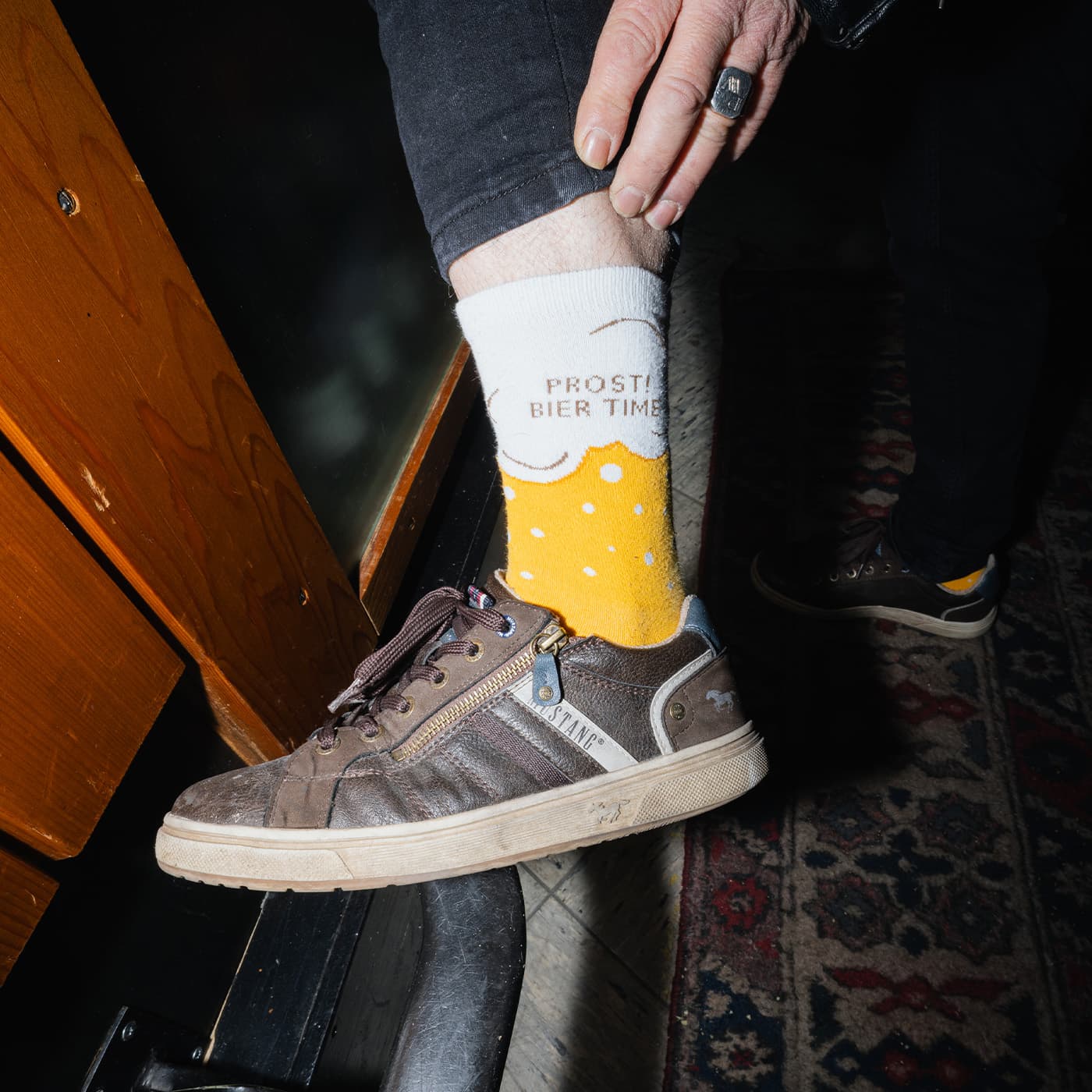 Eine Person zeigt gelbe Socken mit weißen Punkten und PROST! BIER TIME! und trägt getragene Turnschuhe und einen Ring.