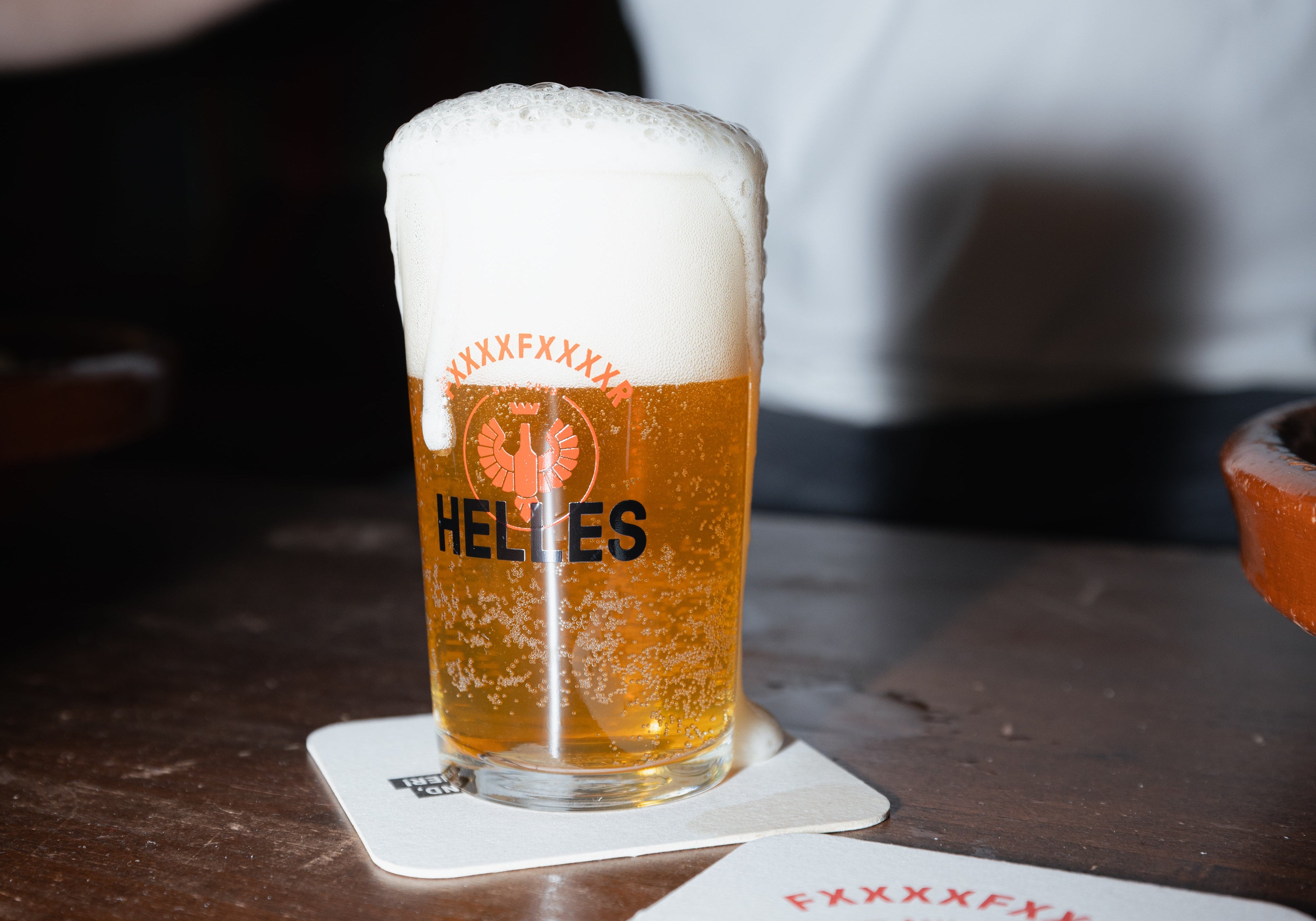 Ein Glas Helles mit einer dicken Schaumkrone steht auf einem Untersetzer auf einem Holztisch.